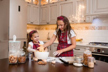 İki küçük kız mutfakta Noel için zencefilli kurabiye pişiriyor.