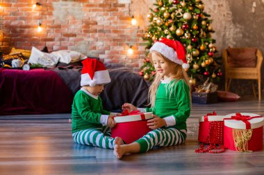 Pijamalı ve Noel şapkalı iki çocuk Noel hediyelerini odaya boşaltın.