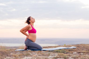 Genç hamile kadın dışarıda yoga yapıyor. Gün batımında yoga.