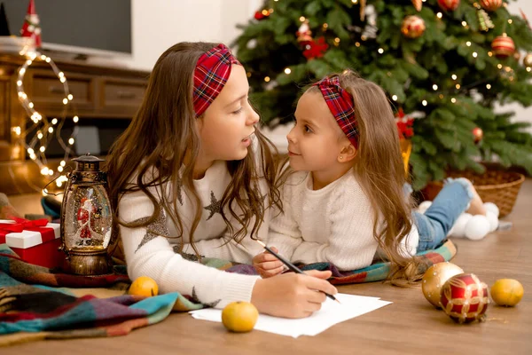 Δύο Κορίτσια Στο Ξύλινο Πάτωμα Του Σπιτιού Δίπλα Στο Χριστουγεννιάτικο — Φωτογραφία Αρχείου