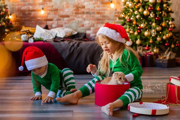 两个身穿睡衣 头戴圣诞帽的小孩在房间里打开了圣诞礼物的包装 — 图库照片