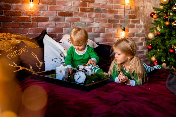 两个穿睡衣的孩子在圣诞树旁边的床上吃早餐 — 图库照片