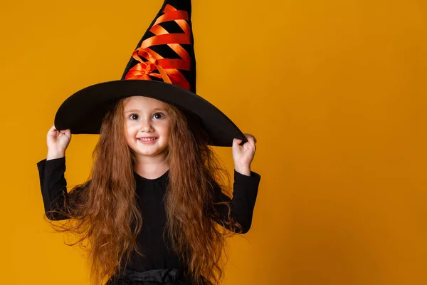 黄色の背景にハロウィンの魔女の衣装に長い赤い髪の少女 子供のためのハロウィーン テキストのためのスペース — ストック写真