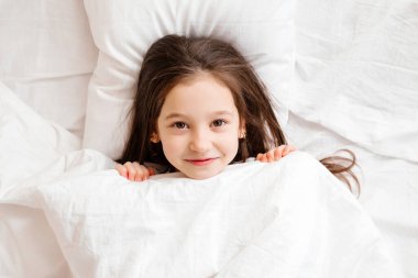 Mutlu küçük kız sabahları yatağında yatıyor. sağlıklı bebek uykusu. beyaz yatak çarşafları, metin için boşluk