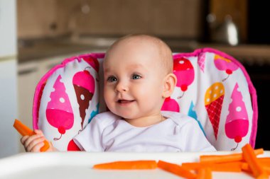 Sevimli küçük bebek renkli bebek koltuğunda yemek yiyor.