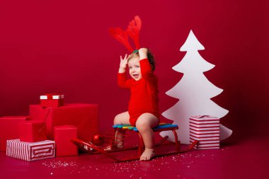 Kafasında geyik boynuzları olan sevimli bir çocuk Noel hediyeleriyle bir kızağın üzerinde oturuyor. yakınlık kavramı, metin için boşluk