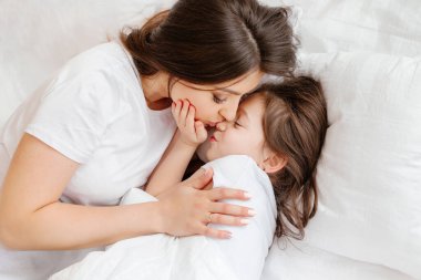 Mutlu genç anne küçük kızını yatakta kucaklıyor, yukarıdan bir manzara. Anne ve kızı evde dinleniyor. Günaydın.!