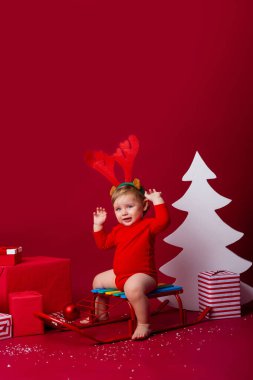 Kafasında geyik boynuzları olan sevimli bir çocuk Noel hediyeleriyle bir kızağın üzerinde oturuyor. yakınlık kavramı, metin için boşluk