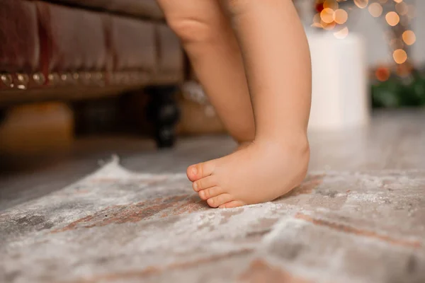 Toddler's feet on the wooden floor next to the Christmas tree, close-up