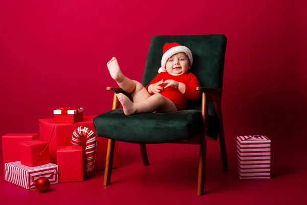 Söt Baby Santa Sitter Stol Bland Julklappar Röd Bakgrund Julkoncept — Stockfoto