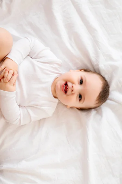 健康的男婴 10个月大 身穿白色衣服 笑着坐在床上的白色床单上 留着文字 — 图库照片