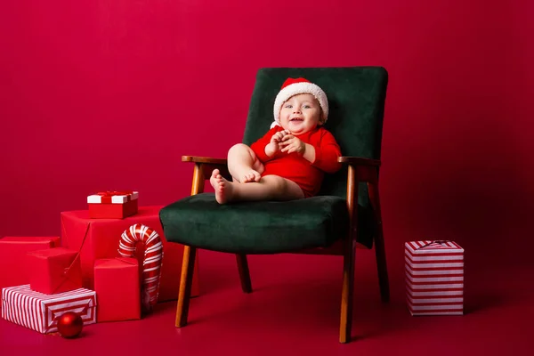 Söt Baby Santa Sitter Stol Bland Julklappar Röd Bakgrund Julkoncept — Stockfoto