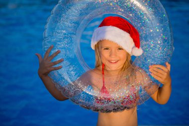 Noel şapkalı küçük kız havuz kenarında yüzme çemberi tutuyor.