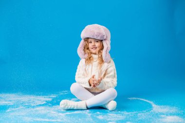 Mavi sırtında sahte karla kışın giyinmiş mutlu küçük kız.