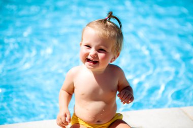 Küçük kız parlak gün ışığında havuz kenarında oturuyor.