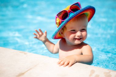 little toddler girl in swimming pool wearing ranbow hat and glasses on it clipart