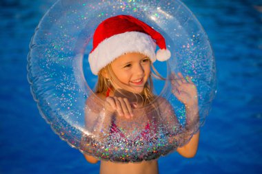 Noel şapkalı küçük kız havuz kenarında yüzme çemberi tutuyor.