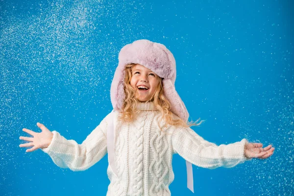 cute little girl in pink furry hat playing with fake snow on blue background in studio