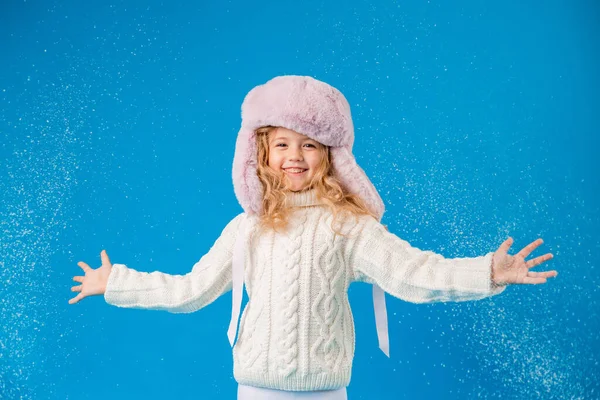 cute little girl in pink furry hat with fake snow on blue background in studio