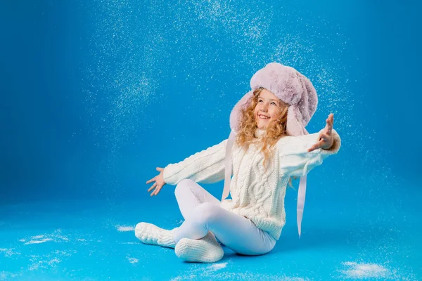 可愛いです女の子でピンク毛皮の帽子遊びますともに偽雪の上に青の背景でスタジオ — ストック写真