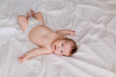 Küçük çocuk beyaz çarşaflarda yatıyor.