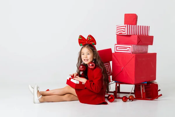 asian girl with bow on head posing with many gifts on white studio background