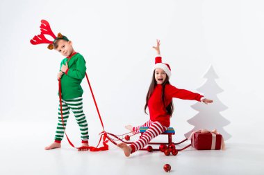 Geyik boynuzlu çocuk kızakta Noel Baba şapkası takan bir kız taşıyor.