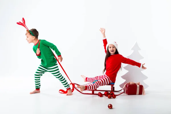 Brother Deer Horns Carrying Happy Sister Wearing Santa Hat Sleigh — Stockfoto
