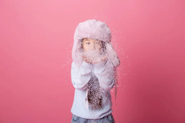可爱的亚洲小女孩 戴着冬季帽子 用粉红的背景把手中的雪吹掉 — 图库照片