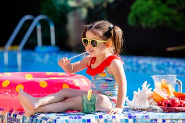 Güneş gözlüklü ve bikinili tatlı esmer kız havuz kenarında limonata içiyor. Çocuk konseptinin yaz tatili