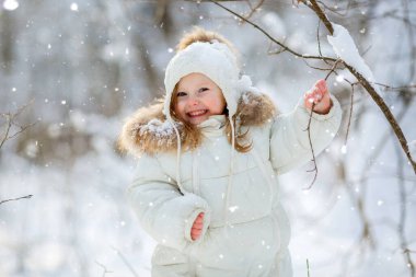 Karlı ormanda, kalın giysiler içinde küçük tatlı bir kız.