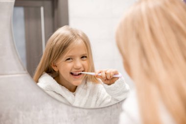 Banyoda dişlerini yıkayan bornozlu tatlı bir kız. 