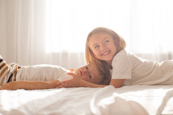 Cute brother and sister lying on bed at home interior 
