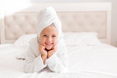 Kafasında havluyla yatağa uzanmış gülümseyen kız.