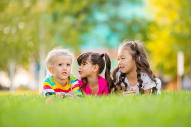 Yazın çimlerin üzerinde Asya, Hindistan ve Avrupa kökenli üç küçük kız yatıyor. Uluslararası Çocuk Günü