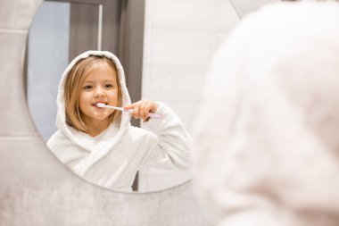 Banyoda dişlerini yıkayan bornozlu tatlı bir kız. 