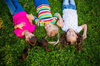 Asya, Hint ve Avrupalı etnik ırkların üç küçük kızı yaz parkında çimlerin üzerinde yatıyor. Uluslararası Çocuk Günü