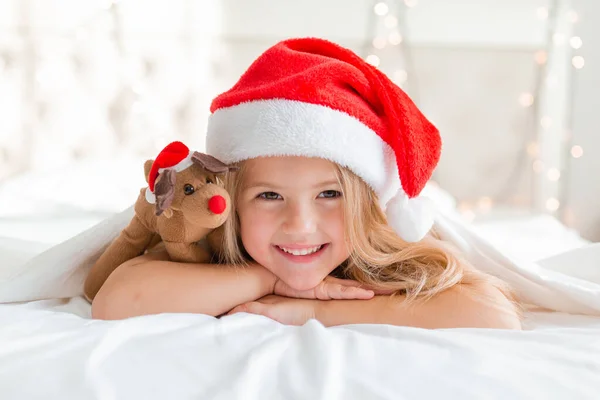 Χαμογελαστό Κοριτσάκι Που Φοράει Καπέλο Γιου Βασίλη Ξαπλωμένο Στο Κρεβάτι — Φωτογραφία Αρχείου
