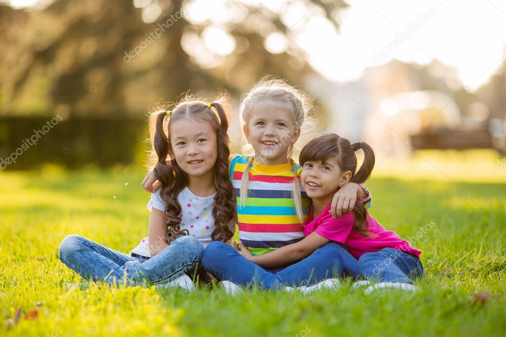 Three little girls cuddle on summer lawn. International Children's Day