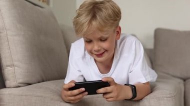 Kanepede akıllı telefonuyla oturan tatlı sarışın çocuk. Çocuklar ve aletler.. 