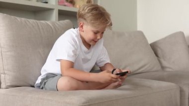 Kanepede akıllı telefonuyla oturan tatlı sarışın çocuk. Çocuklar ve aletler.. 