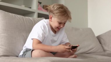 Kanepede akıllı telefonuyla oturan tatlı sarışın çocuk. Çocuklar ve aletler.. 