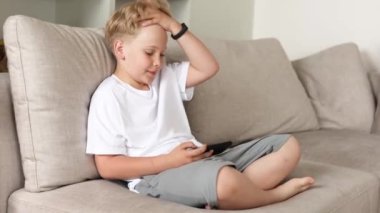 Kanepede akıllı telefonuyla oturan tatlı sarışın çocuk. Çocuklar ve aletler.. 