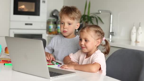 两个年幼的男孩和女孩坐在厨房的桌旁 一边看卡通片 一边用笔记本电脑笑 儿童和小玩艺儿 — 图库视频影像