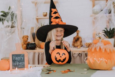 Elinde balkabağı şeklinde bir sepet tutan cadı şapkalı, uzun saçlı küçük sarışın bir kızın portresi. Cadılar Bayramı konsepti Mesaj için yer var. Yüksek kalite fotoğraf