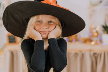 Elinde balkabağı şeklinde bir sepet tutan cadı şapkalı, uzun saçlı küçük sarışın bir kızın portresi. Cadılar Bayramı konsepti Mesaj için yer var. Yüksek kalite fotoğraf