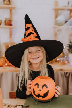 Elinde balkabağı şeklinde bir sepet tutan cadı şapkalı, uzun saçlı küçük sarışın bir kızın portresi. Cadılar Bayramı konsepti Mesaj için yer var. Yüksek kalite fotoğraf