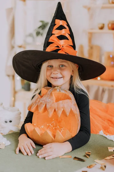 一个金发碧眼的小女孩的画像 她穿着巫婆服装 戴着巨大的巫婆帽 手里拿着一个南瓜形的糖果篮 万圣节的概念 文字空间 高质量的照片 — 图库照片