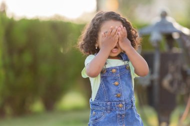 Koyu tenli, kot elbiseli kıvırcık saçlı küçük bir kız güneşli bir günde parkta yürüyor. Sağlıklı yaşam tarzı kavramı. Mutlu çocukluk