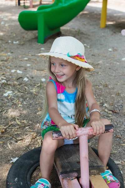 Alegre niña en un sombrero balanceándose en un viejo columpio — Foto de Stock